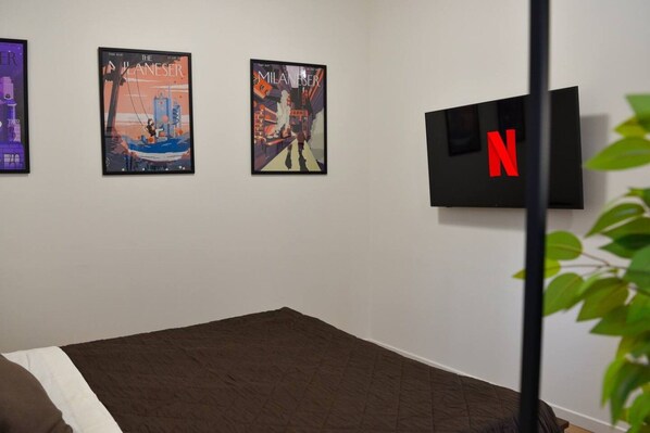 A room with a bed, a TV mounted on the wall, and two framed posters on the wall.