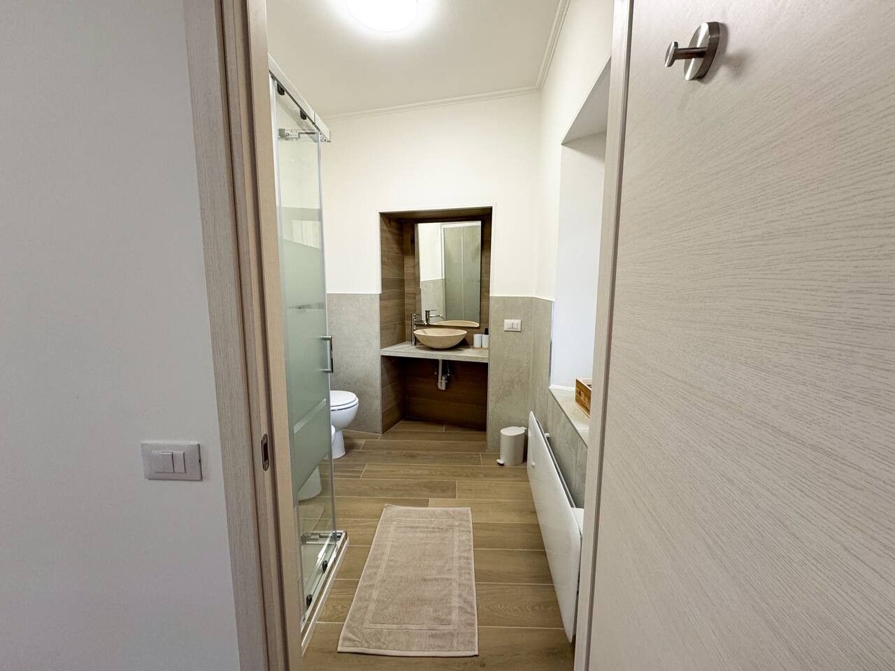 Un corridoio stretto che conduce a un bagno con lavandino, WC e specchio.