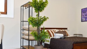 A bedroom with a bed, pillows, a bedside table, a nightstand, a potted plant, and a wall-mounted shelf with cushions. - Fly&Rest MXP | Suite | Airport Transfer 24/7 (Casorate Sempione)