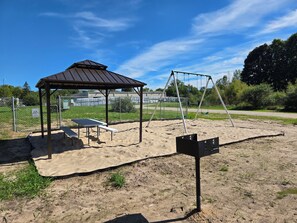 Un'area all'aperto sabbiosa con un riparo in metallo, altalene e un tavolo da picnic.