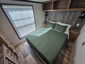 A bedroom with a bed, a nightstand, a window with blinds, and a wooden floor.