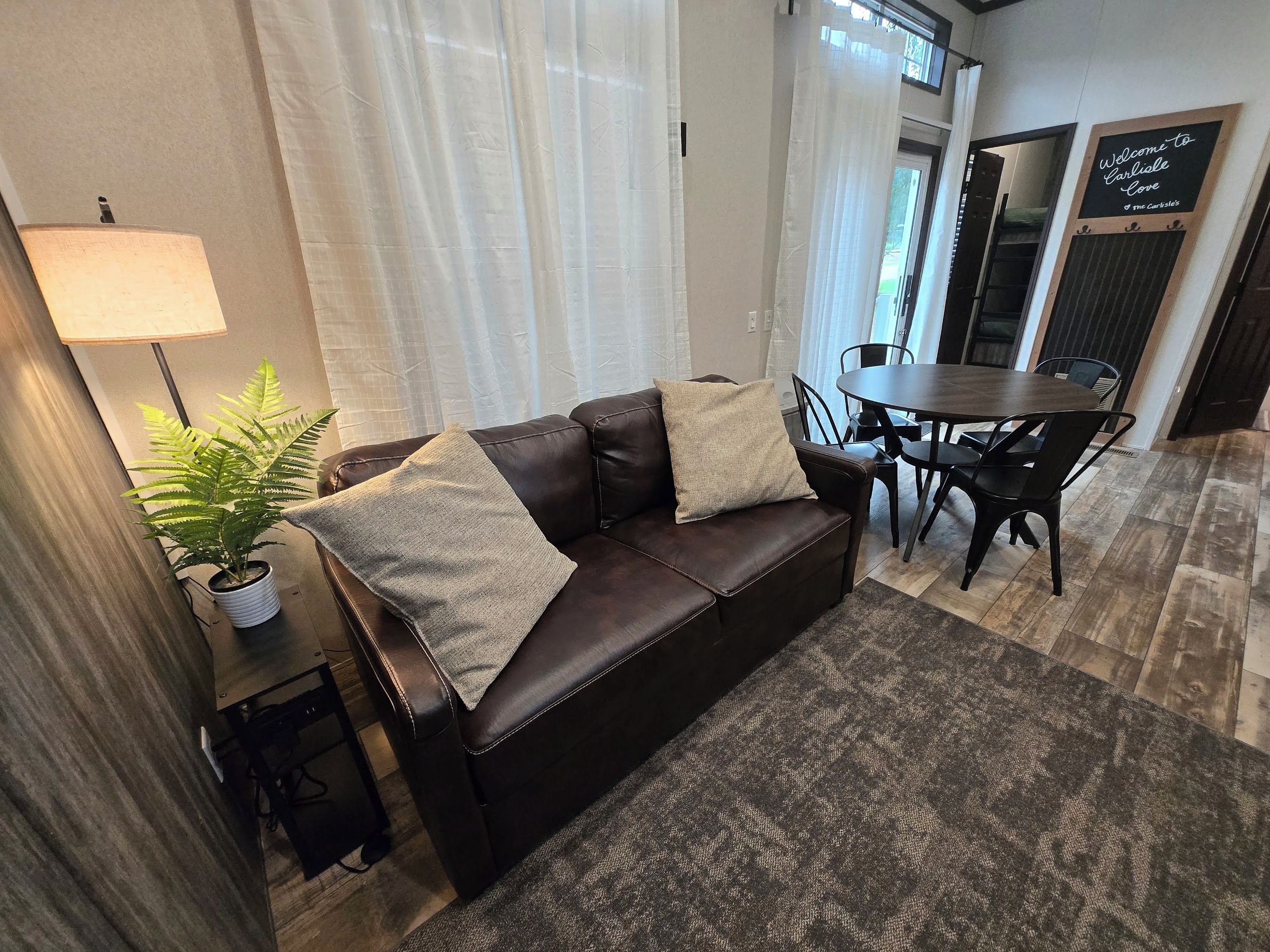 A furnished living room with a leather sofa, a dining table, chairs, a potted plant, and a lamp.