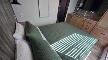 A bedroom with a bed, a nightstand, a wall-mounted lamp, a door, and a TV on a wooden cabinet.