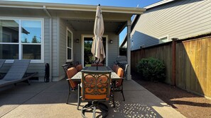 Une terrasse extérieure avec une table et des chaises, un barbecue et un espace abrité agrémenté de guirlandes lumineuses.