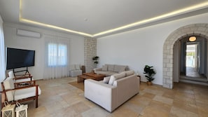 A modern living room with a flat-screen TV, a sofa set, a coffee table, and a stone fireplace. - Milos AquaBliss Beachfront, Milos AquaBliss Beachfront (Milos)