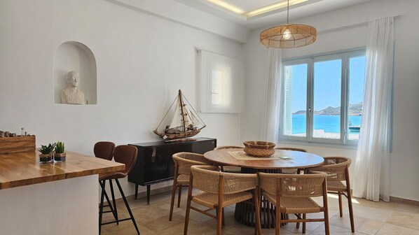 A dining area with a round table, wicker chairs, and a ship model. - Milos AquaBliss Beachfront, Milos AquaBliss Beachfront (Milos)