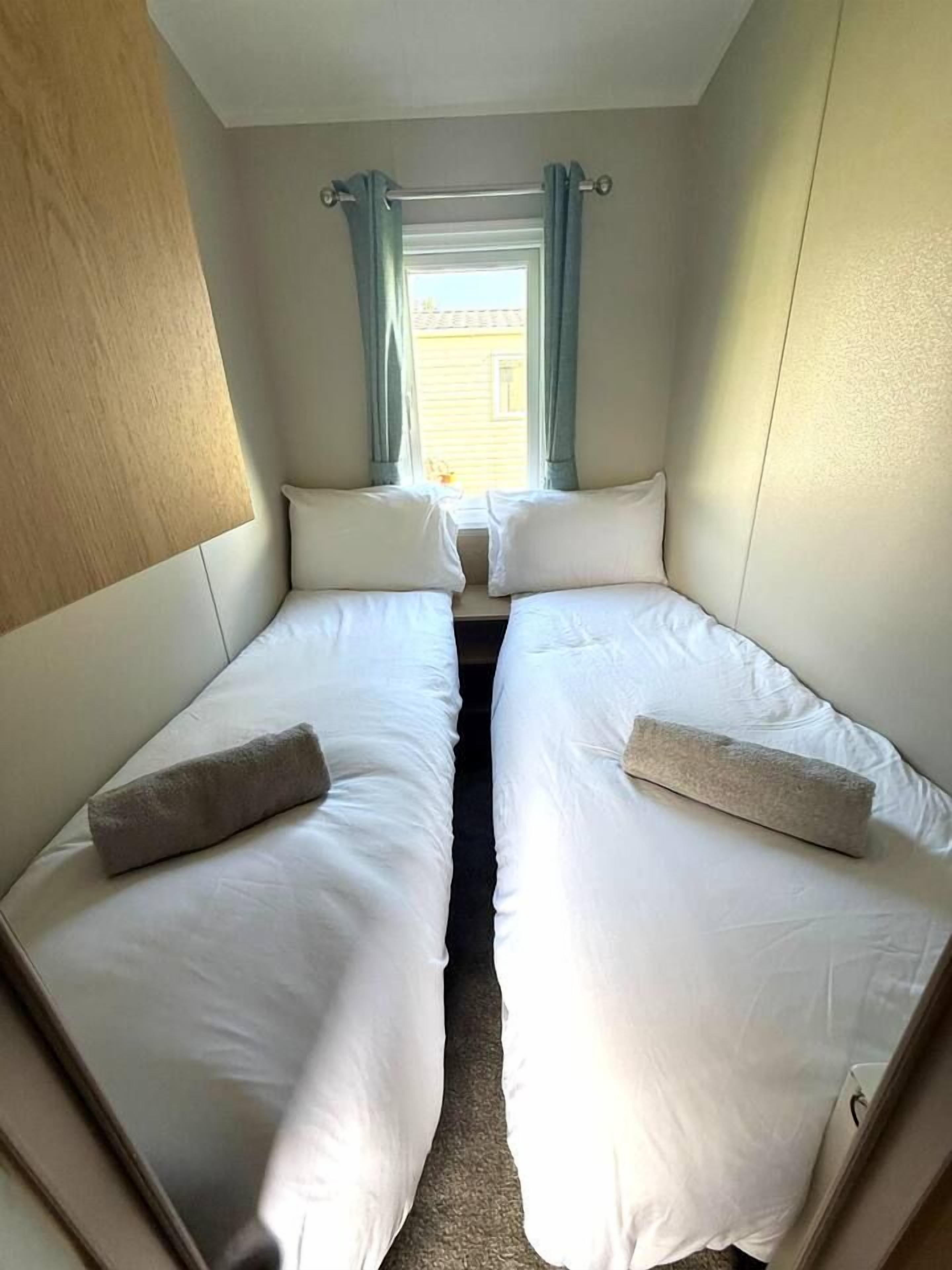 A compact room with two single beds, a window with curtains, and a view of a building outside.