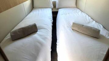 A compact room with two single beds, a window with curtains, and a view of a building outside.