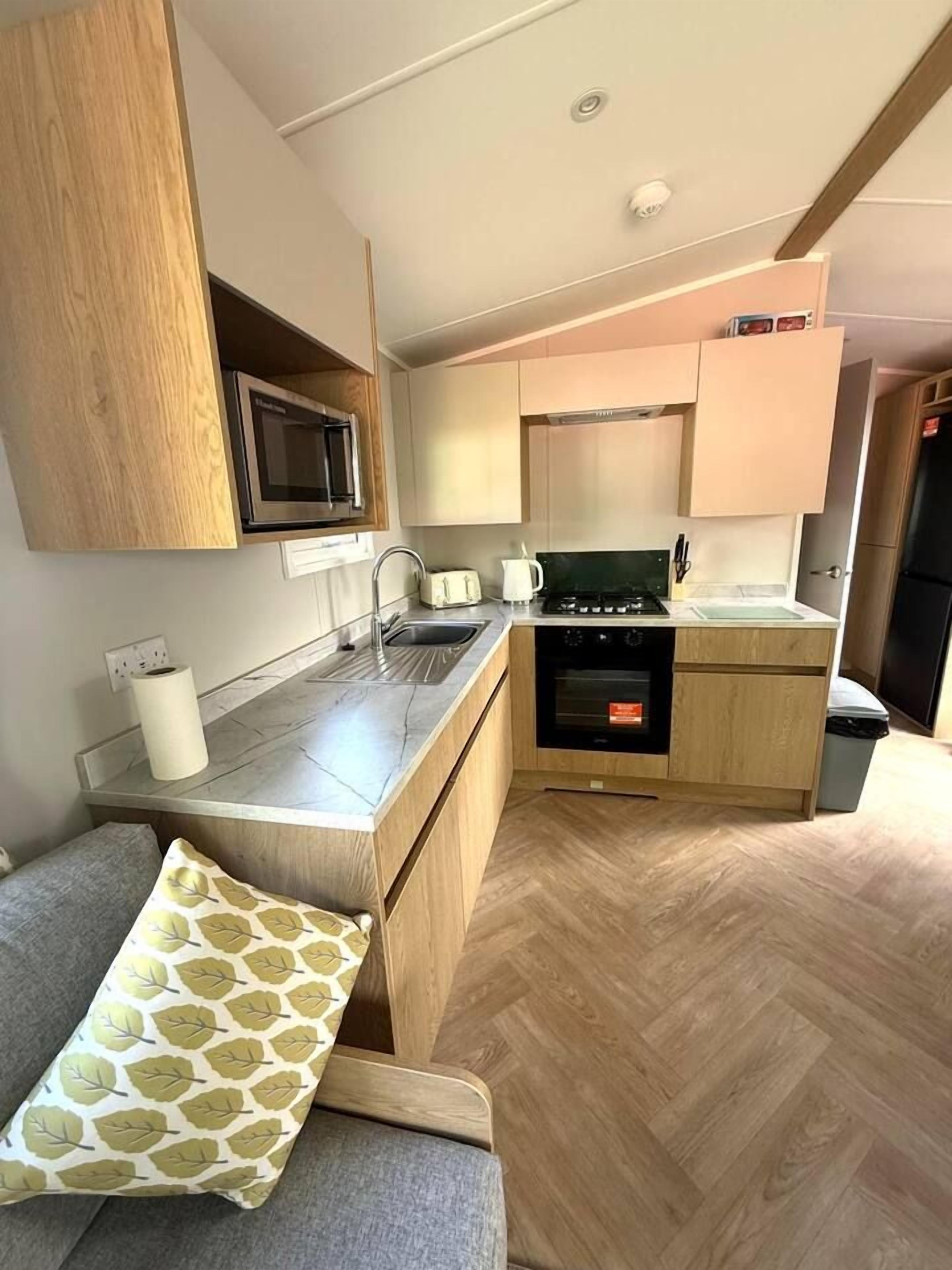 A compact kitchen with a microwave, stove, sink, and wooden cabinets.