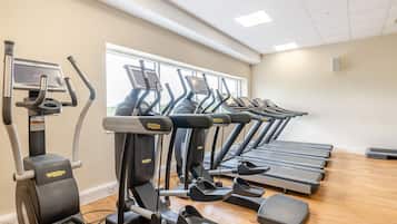 A gym with multiple treadmills and elliptical machines, wooden flooring, and a large window providing natural light.