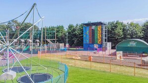 Zona de jocs amb un mur de paret, balançadors i un àrea tancada amb un trampolí.