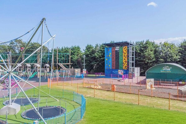 A playground with a climbing wall, a swing set, and a fenced area with a trampoline.