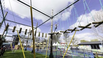 An outdoor adventure course with ropes, poles, and a fenced area.