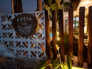 A sign with the name 'AREIA' and a logo, set against a decorative white metal fence with vertical wooden slats.
