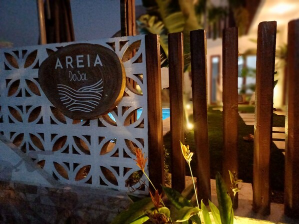 Une enseigne portant le nom « AREIA » et un logo, placée devant une clôture décorative en métal blanc, composée de lattes de bois verticales.