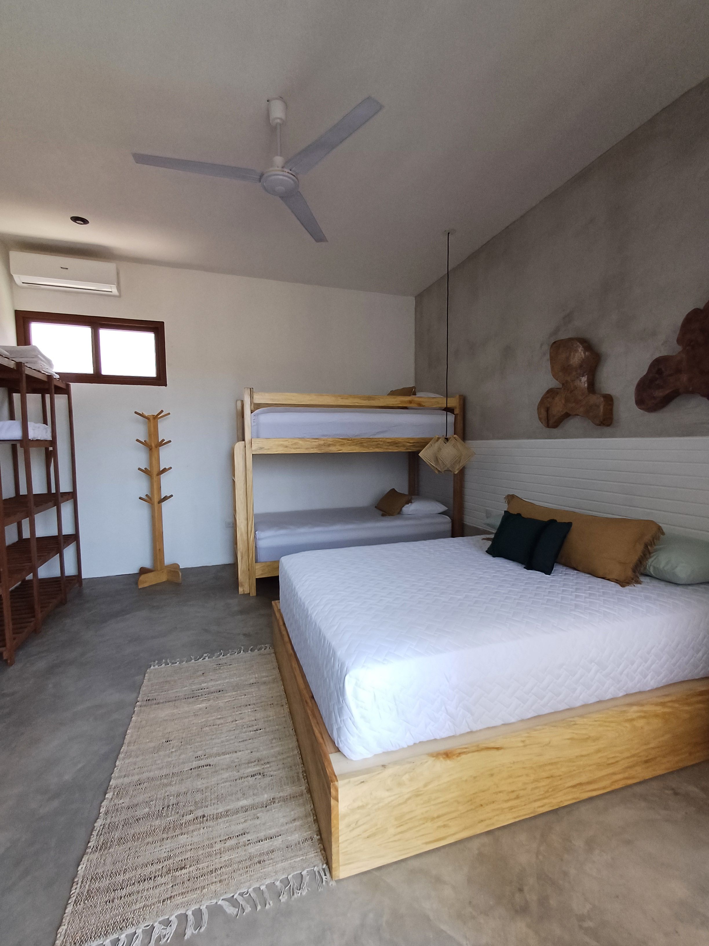 Un dormitorio con una cama litera, ventilador de techo, perchero de madera y ventana.