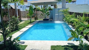 Une piscine rectangulaire bordée de pierres, entourée d’une végétation luxuriante et d’une clôture en bois.