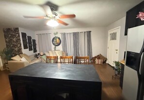 Espaço de refeições com mesa, cadeiras, ventilador de teto e cozinha equipada com geladeira.
