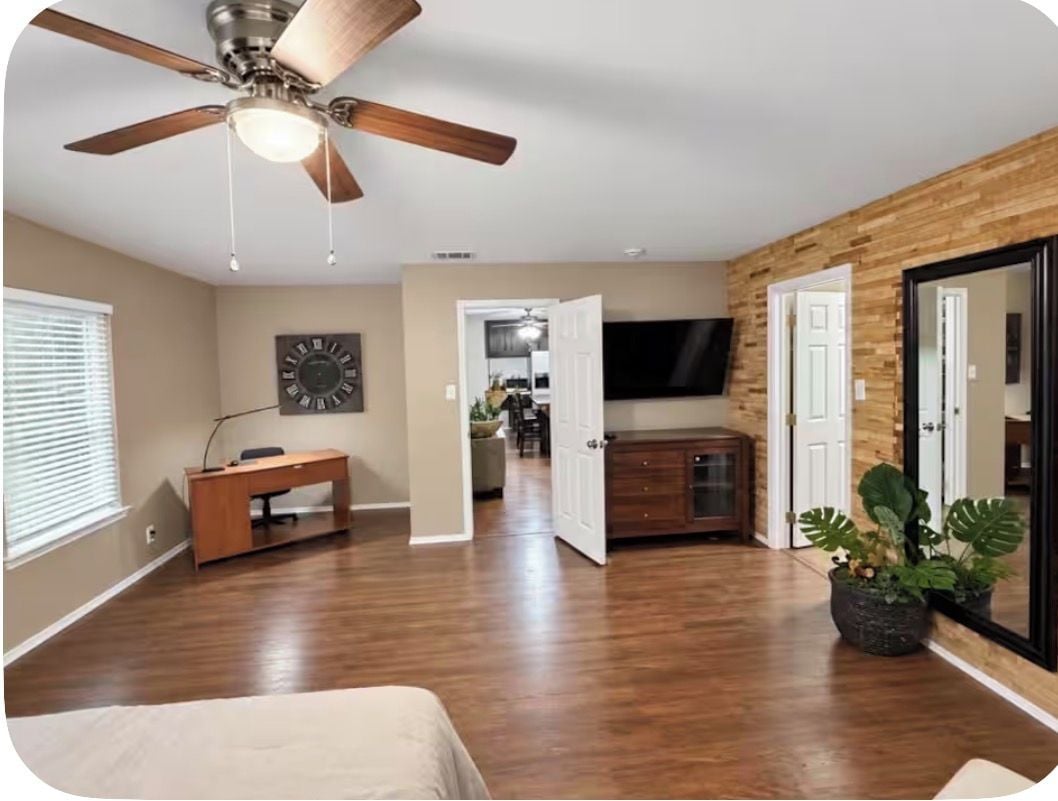 A spacious room with a ceiling fan, a desk, a television, and a large mirror.