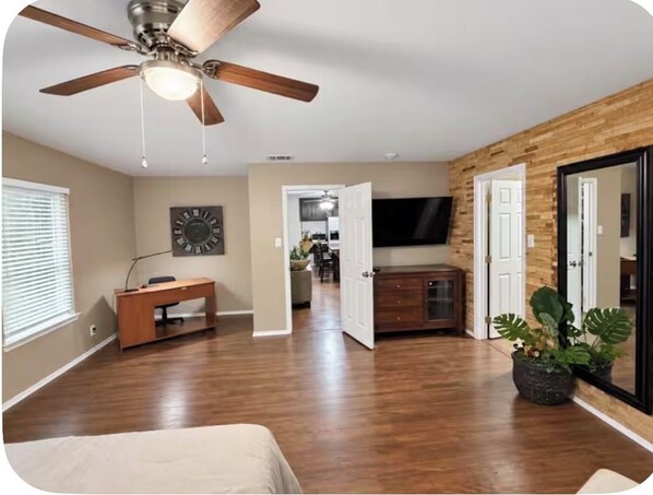 A spacious room with a ceiling fan, a desk, a television, and a large mirror.