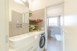 A modern bathroom with a sink, mirror, and a washing machine. - Villa in Tuscany With Pool and Countryside Views (Lucca)