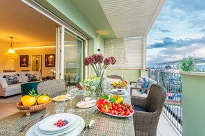 A balcony with a dining table set for a meal, surrounded by wicker furniture and a view of the city. - Villa in Tuscany With Pool and Countryside Views (Lucca)
