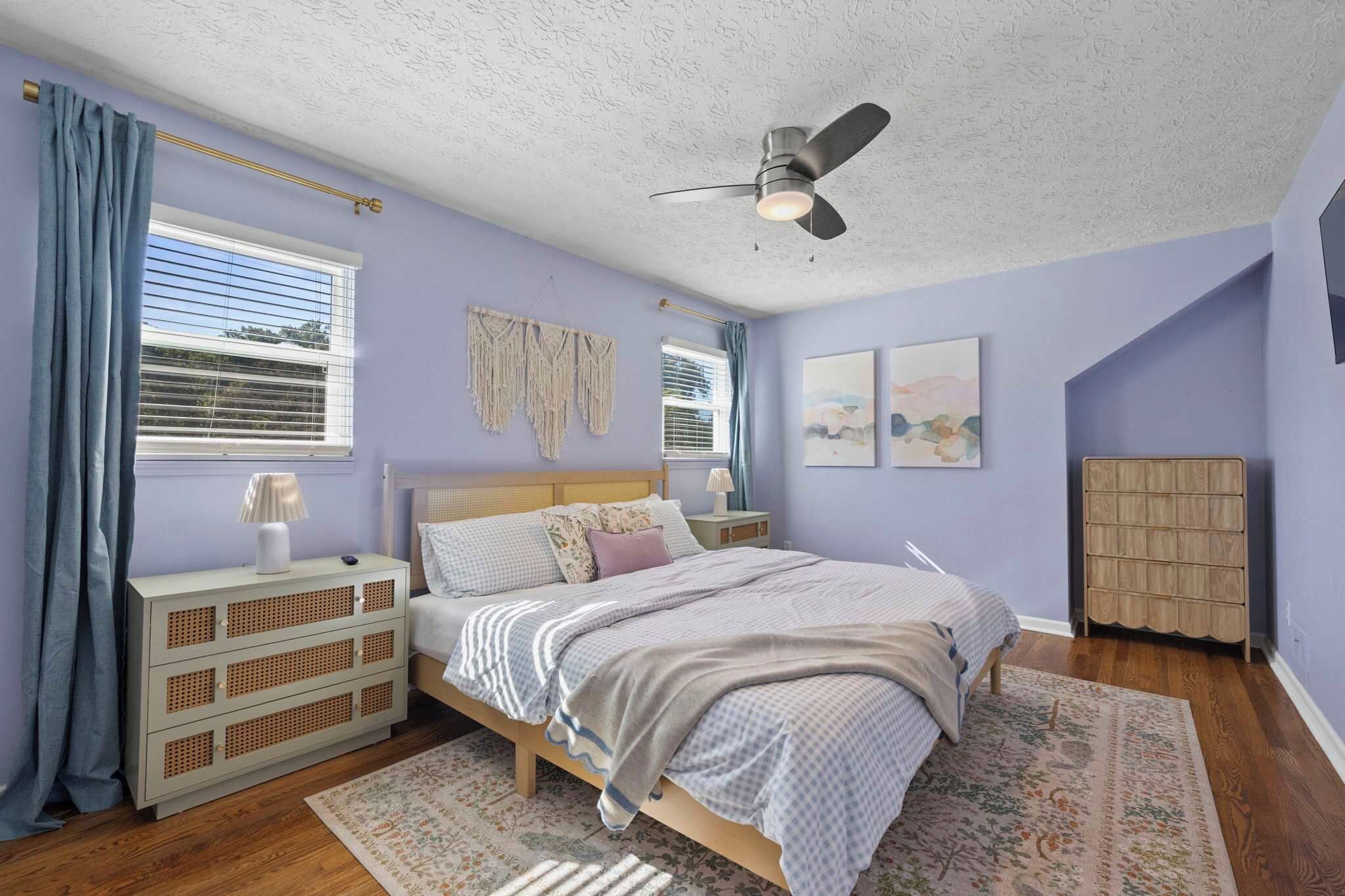 A bedroom with a bed, bedside tables, a ceiling fan, and artwork on the walls.