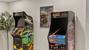 Two arcade machines with colorful graphics and controls, placed in a room with a white wall and a framed picture above them.