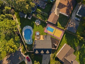 An aerial view of a residential area with a swimming pool, a tennis court, and a hot tub. - Pool, Hot Tub, Pickleball, Sauna, Game Room, Basketball, Fire Pit & Kids Playset (Columbus)