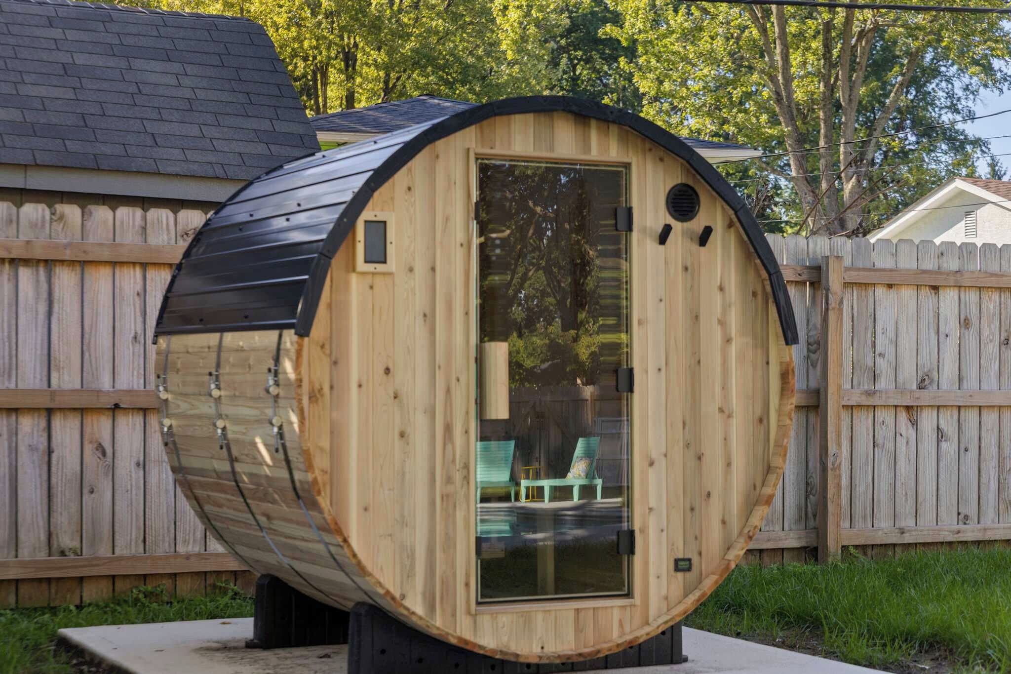 A cylindrical wooden structure with a door, two windows, and a small outdoor seating area with chairs.