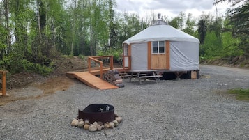 A small, single-story cabin with a covered porch and a fire pit in front.