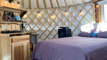 A cozy room with a bed, wooden cabinets, a small table, and a wall-mounted light fixture.