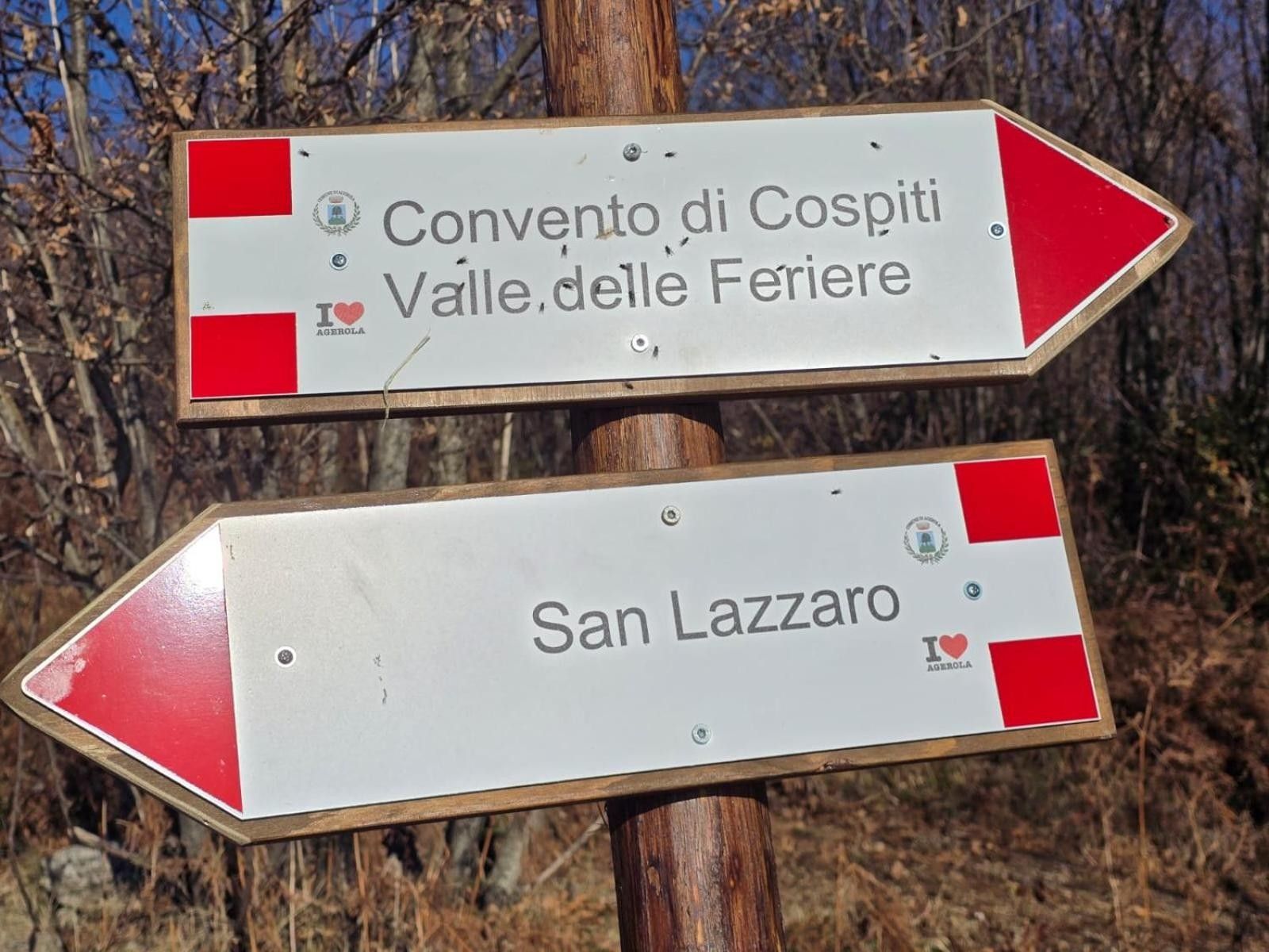 Two directional signs with text, one pointing to 'Convento di Cospiti Valle delle Feriere' and the other to 'San Lazzaro.'