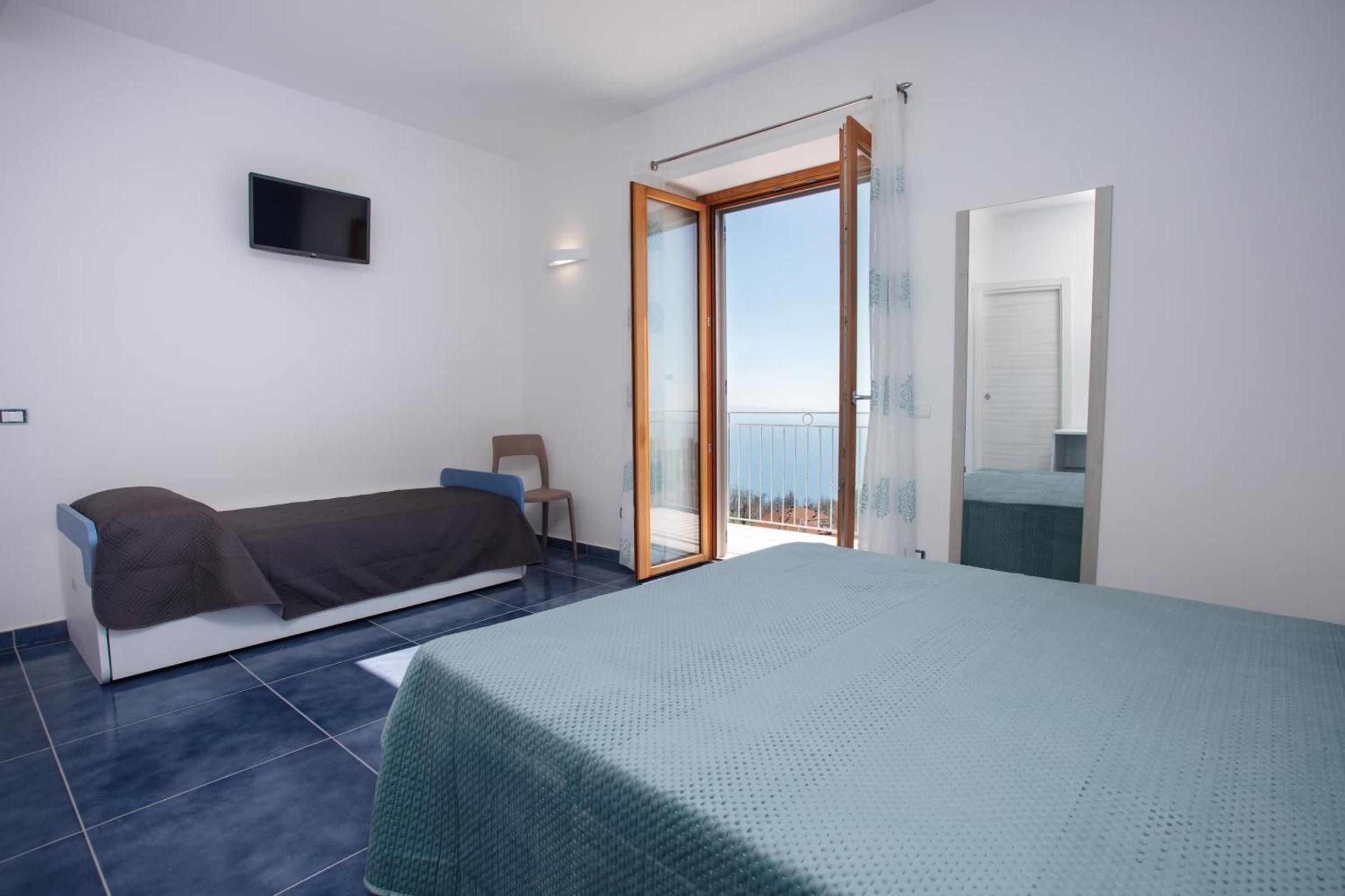 Ein Schlafzimmer mit Bett, Sofa, Fernseher und einem Balkon mit Tür.