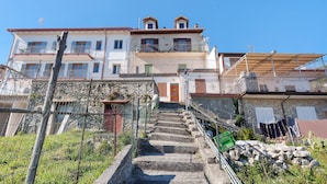 Un edificio a più piani con una scala che conduce a una porta, immerso nel verde e circondato da una recinzione.