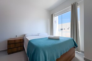 Ein Schlafzimmer mit einem Bett, einem Nachttisch aus Holz und einem Fenster mit Vorhängen.