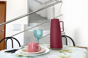 A dining table with a floral tablecloth, a red mug, a blue glass, and a black remote control. - Apartamento 4 com 2 suítes 450m da praia (Santa Cruz Cabrália)