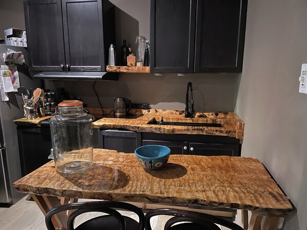 A kitchen with dark cabinets, a wooden countertop, and a coffee maker.