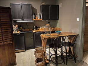 Una cocina compacta con armarios oscuros, encimera de madera y un pequeño comedor con dos sillas.