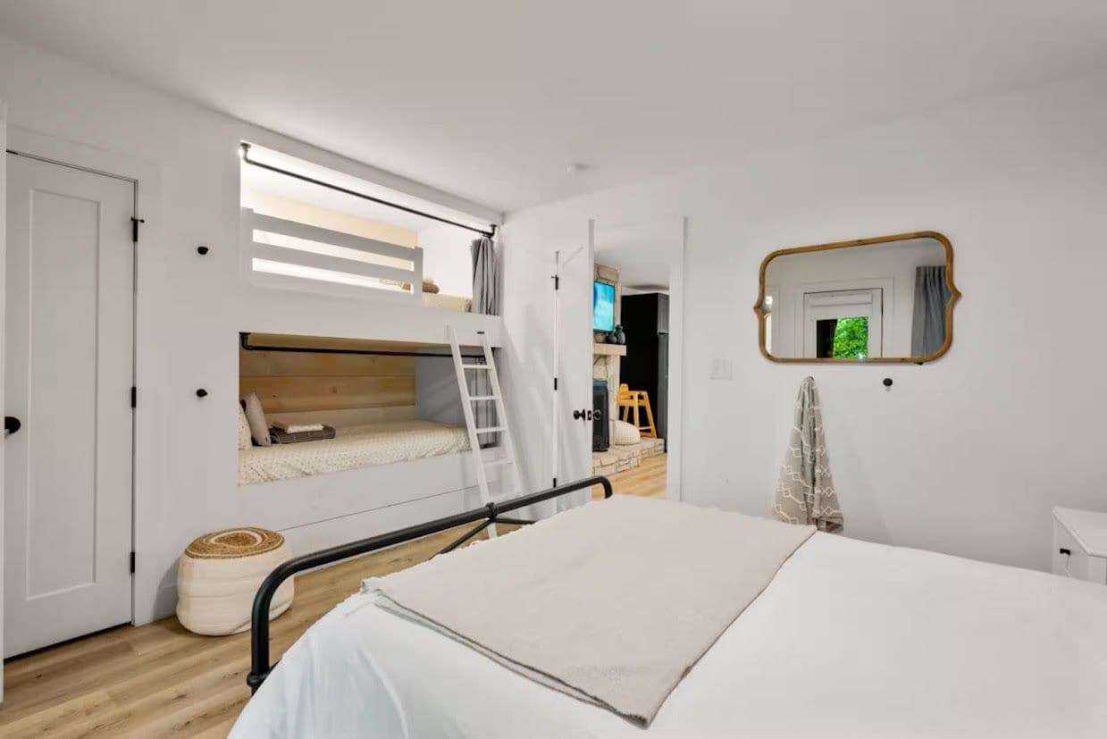 A bedroom with a bunk bed, a single bed, a ladder, a mirror, and a door.