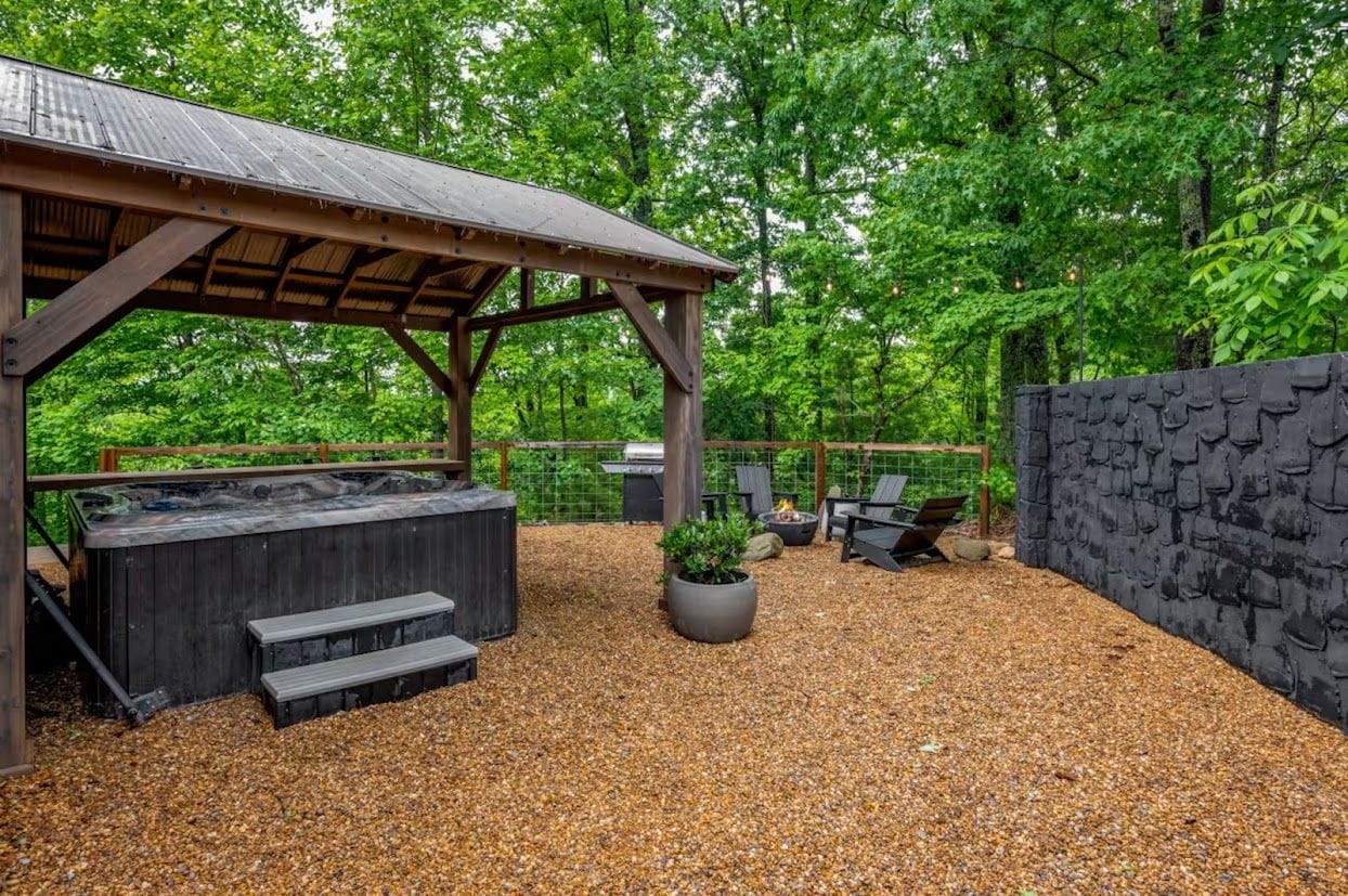 A covered outdoor area with a hot tub, seating, and a stone wall.