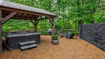 A covered outdoor area with a hot tub, seating, and a stone wall.