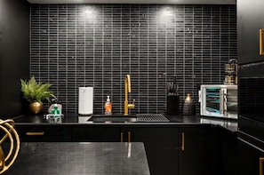 A modern kitchen with black tiles, a gold faucet, and a built-in oven.