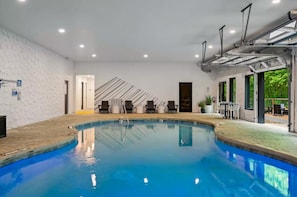 A swimming pool with a tiled deck, lounge chairs, and a modern interior design.