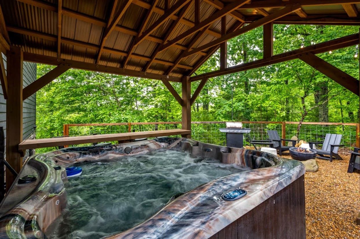 A hot tub area with a wooden deck, surrounded by trees.