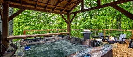 A hot tub area with a wooden deck, surrounded by trees.