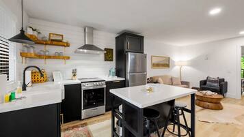 A modern kitchen with white countertops, black cabinetry, and stainless steel appliances. There is a dining area with a white table and stools.