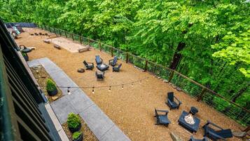 An outdoor patio area with seating and a fire pit, surrounded by dense greenery.