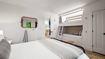 Un dormitorio con una cama litera, una mesita de noche, un espejo y una puerta.