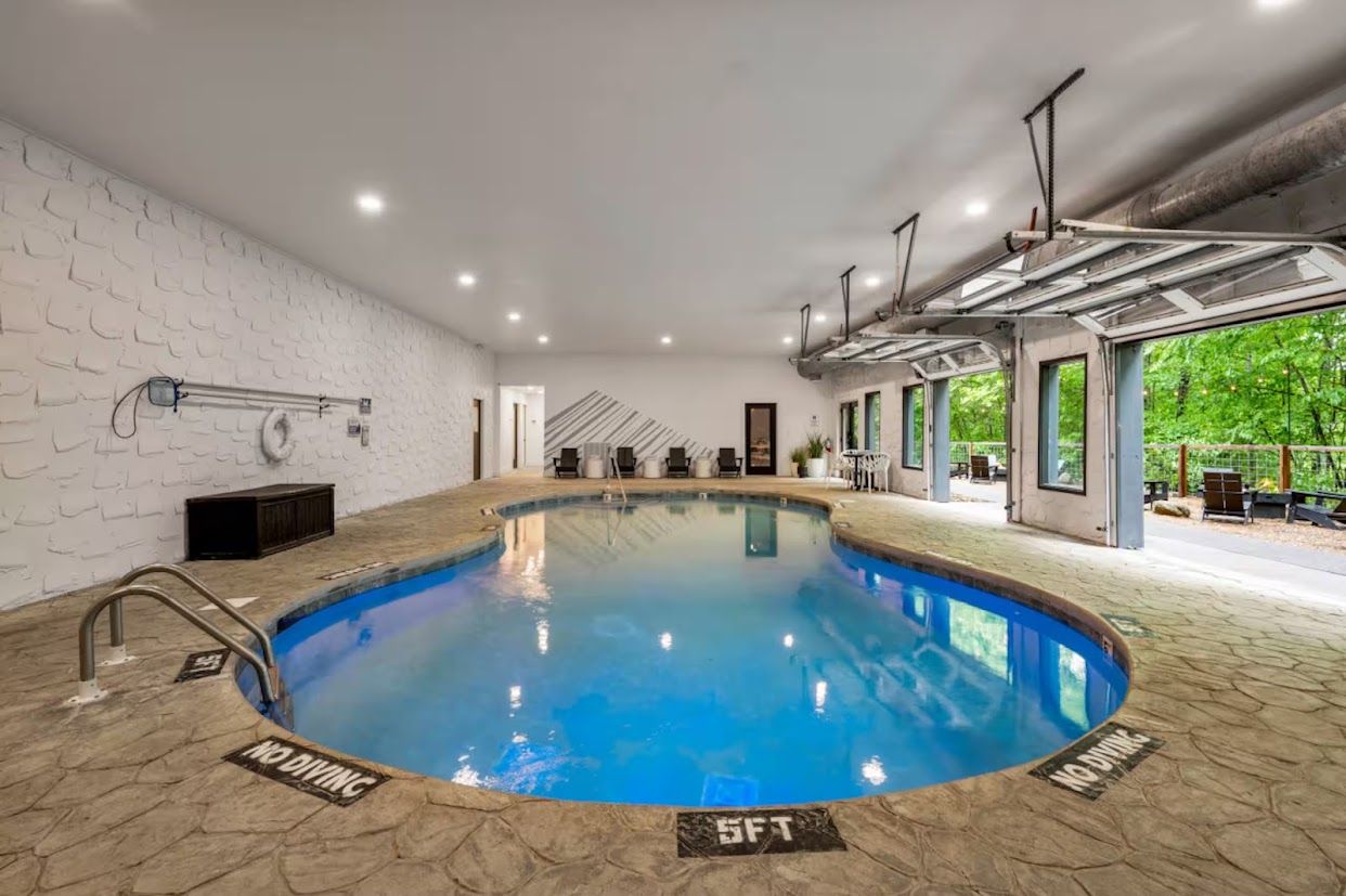 An indoor swimming pool with a no diving sign, a 5ft depth marker, and a view of greenery outside.